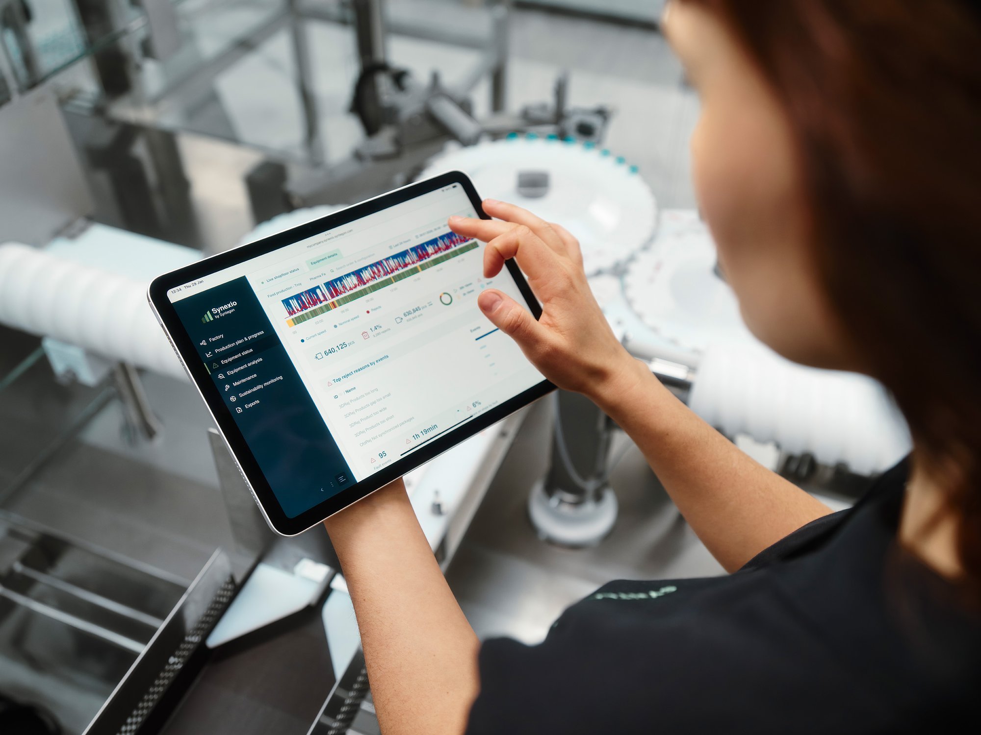 Person using a tablet to monitor digital performance data on a packaging line in an industrial production environment.