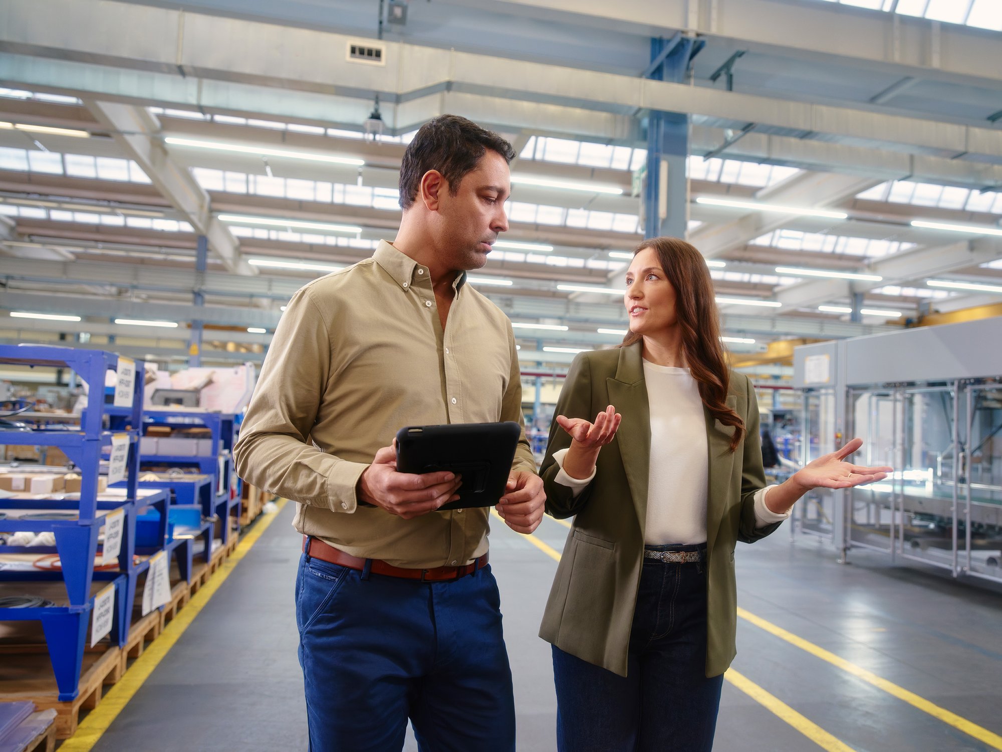 Two professionals walking through a production facility while discussing service and equipment performance with a tablet.