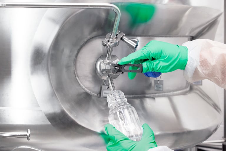 Gloved operator drawing liquid from a stainless steel pharmaceutical vessel, illustrating routine checks and maintenance for reliable formulation.