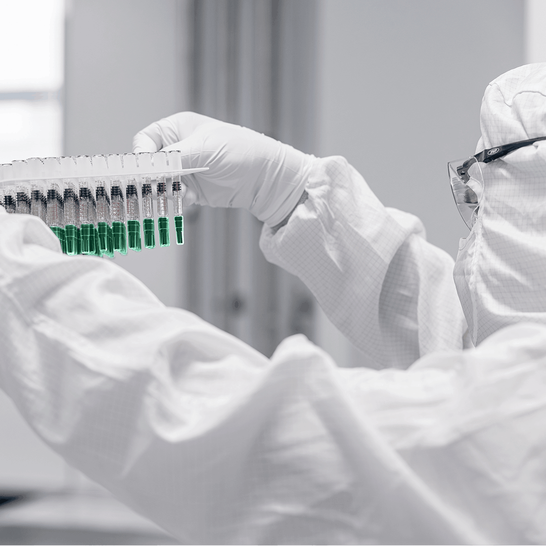 Person in cleanroom gown and gloves holding a nest of ready to use containers with green caps up to the light for visual inspection.