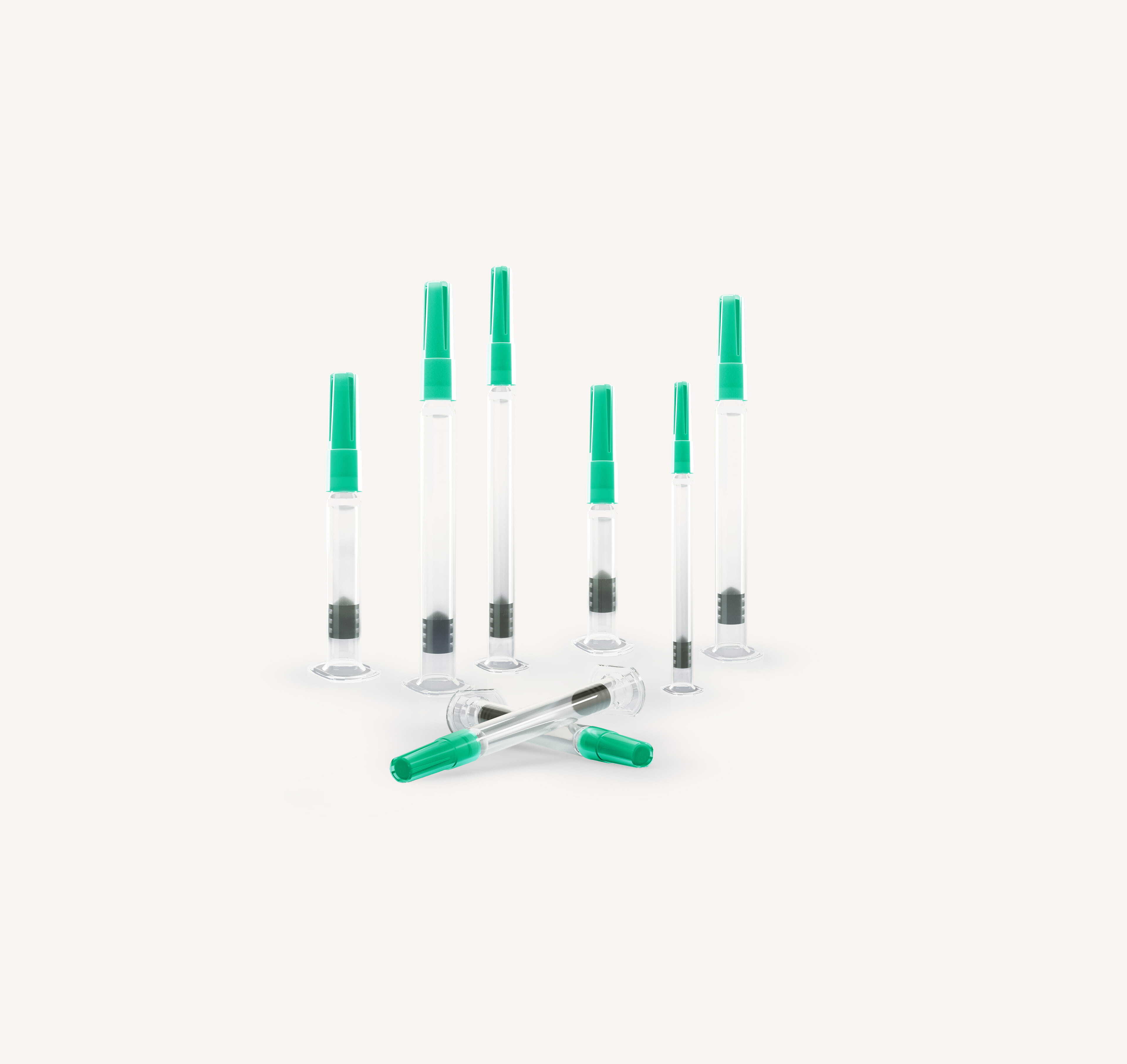 Group of prefilled glass syringes in different sizes with green needle shields arranged upright and lying down.